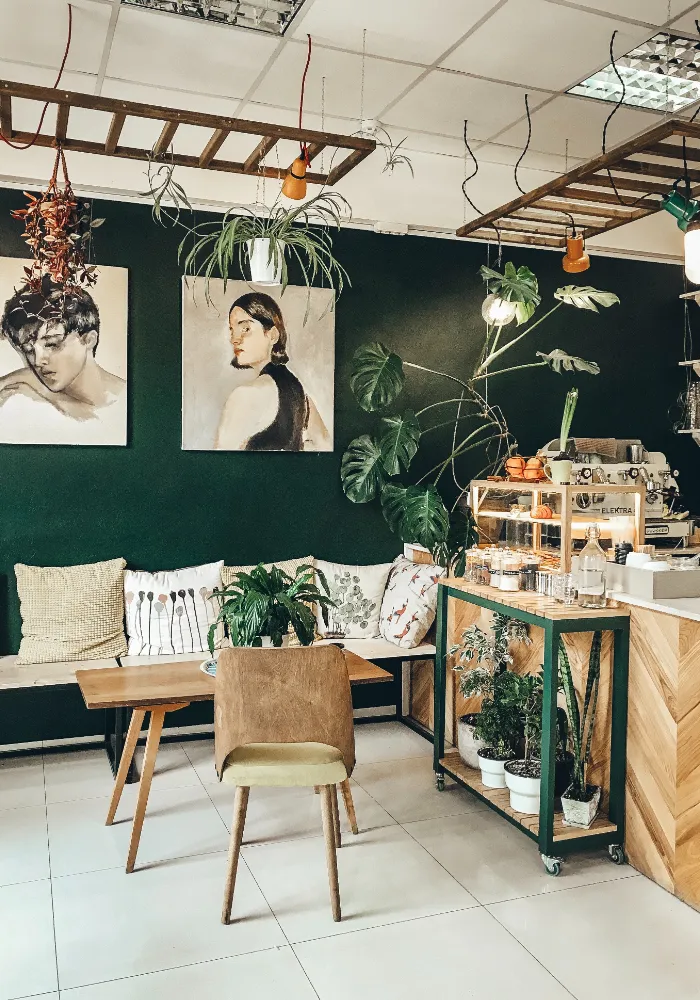 کافه ای که دیوار های آن پر شده از تابلو های نقاشی و در جلو دیوار مبل راحتی و میز عسلی قرار دارد و در کنار مبل بار کافه وجود دارد که در کنارش گل گذاشته شده است